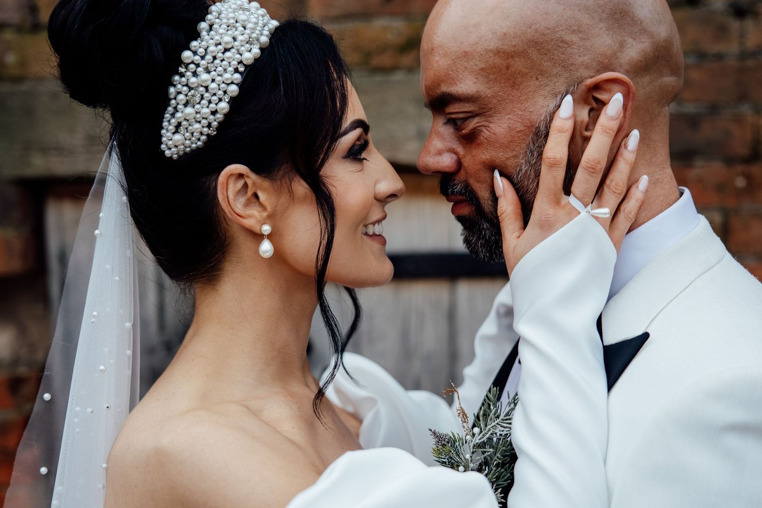 Romantic wedding couple embracing in front of exposed brick wall.