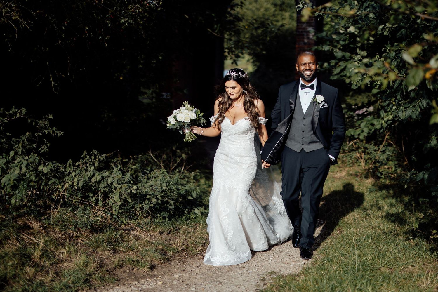 Couple walks together through lush green garden setting during wedding photoshoot.