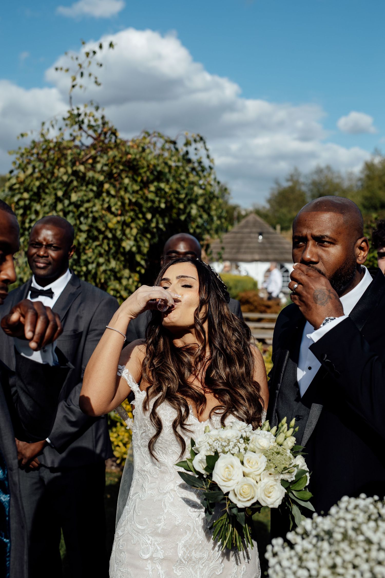 Wedding party laughing and celebrating outdoors with white floral bouquets.