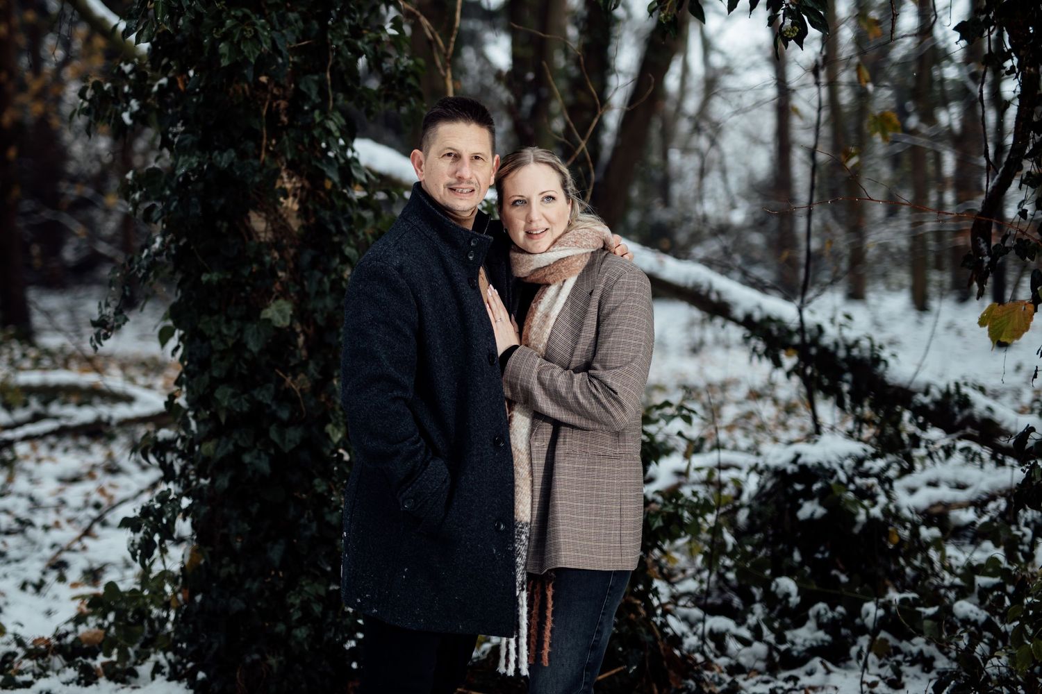 A joyful winter engagement portrait among snow-covered evergreen trees.