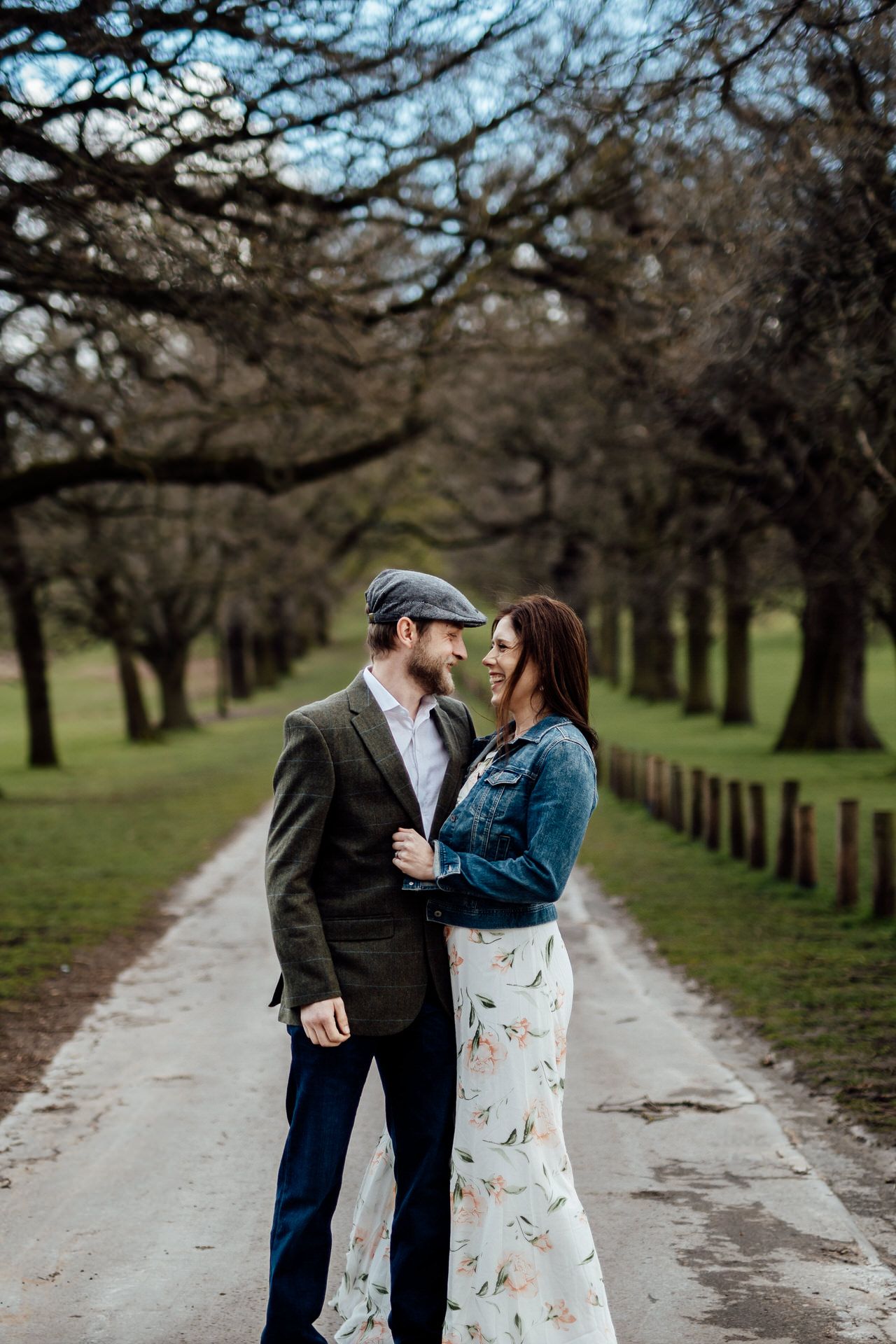Couple shares tender moment on tree-lined pathway in park.
