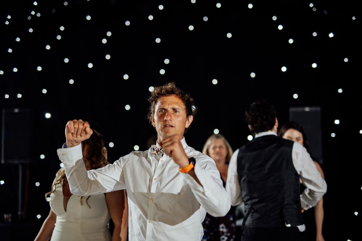 Guests dancing and celebrating at a wedding reception with twinkling lights overhead.