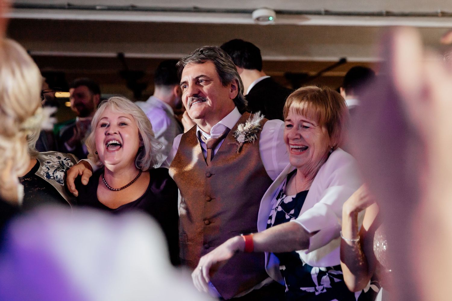 Wedding reception guests dancing and celebrating under purple mood lighting.