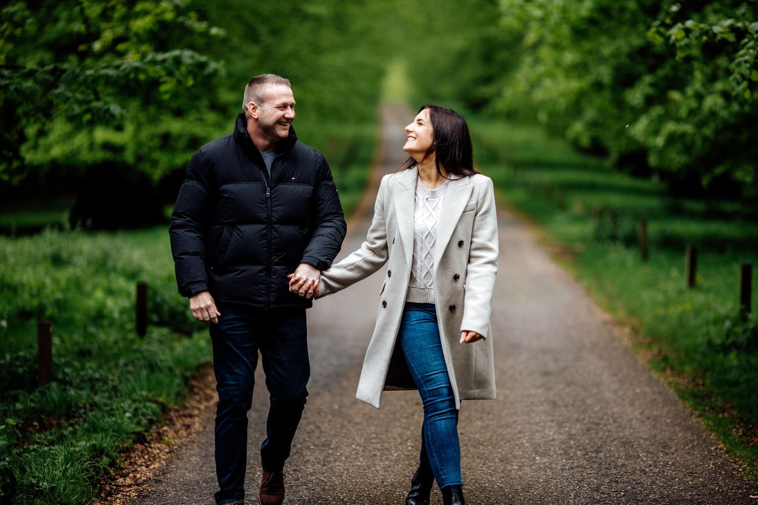 A couple walks hand in hand down a tree-lined path on an autumn day.