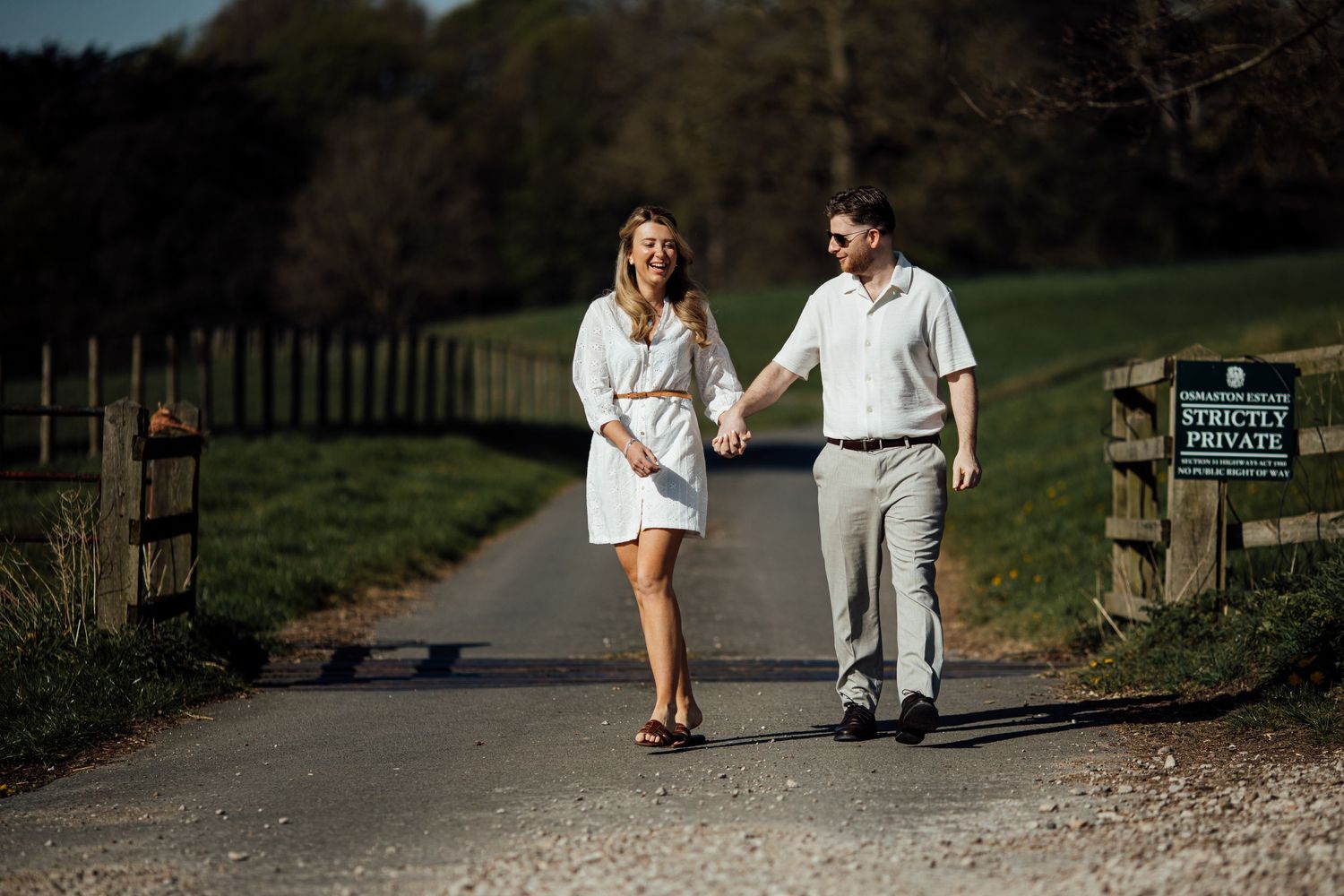A couple takes a romantic stroll along a tree-lined pathway on a sunny day.