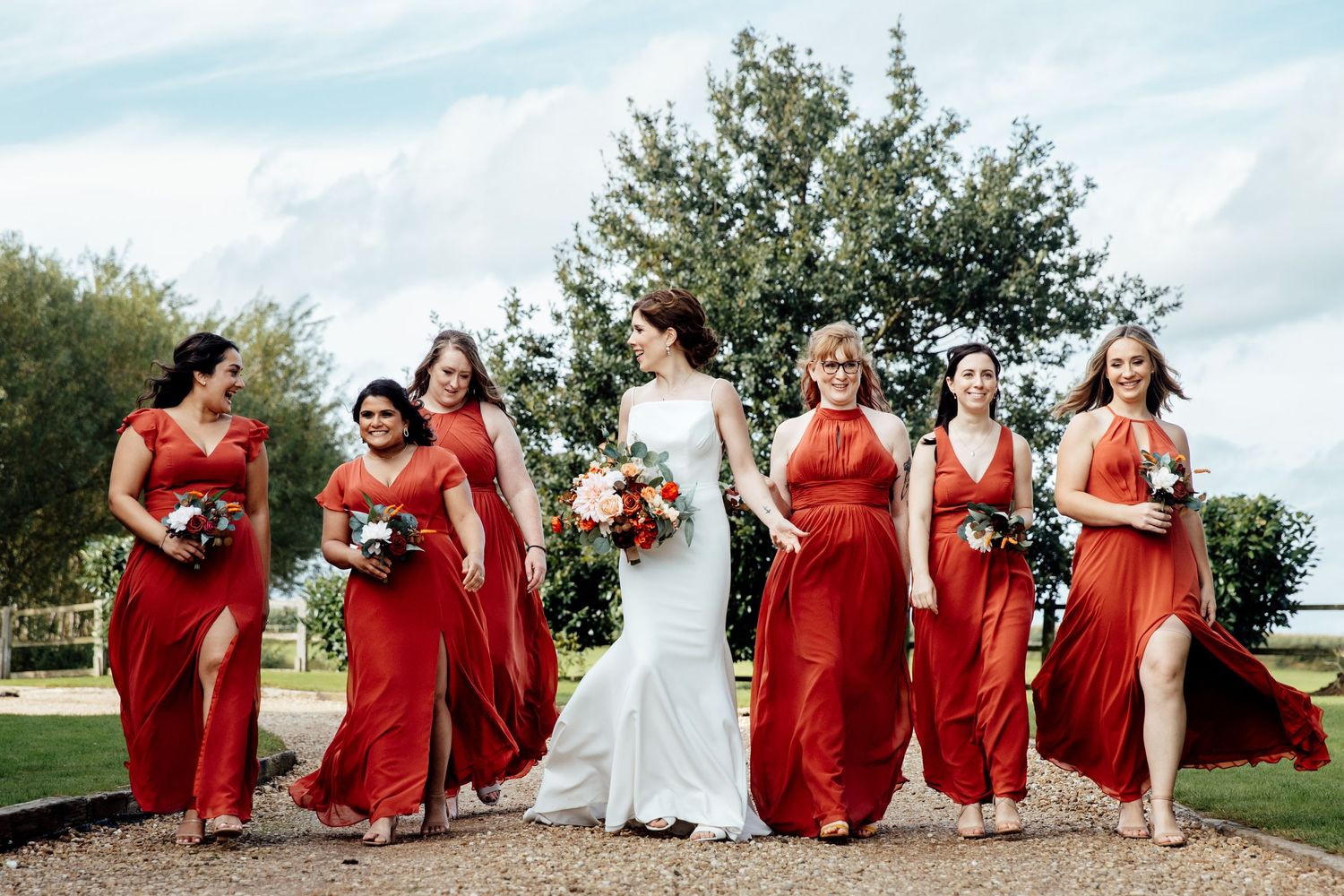 Wedding party in coral red dresses posing together outdoors on a sunny day.