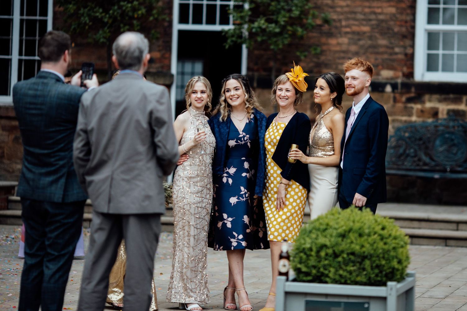 Wedding party gathered outside a brick building with white-framed windows.