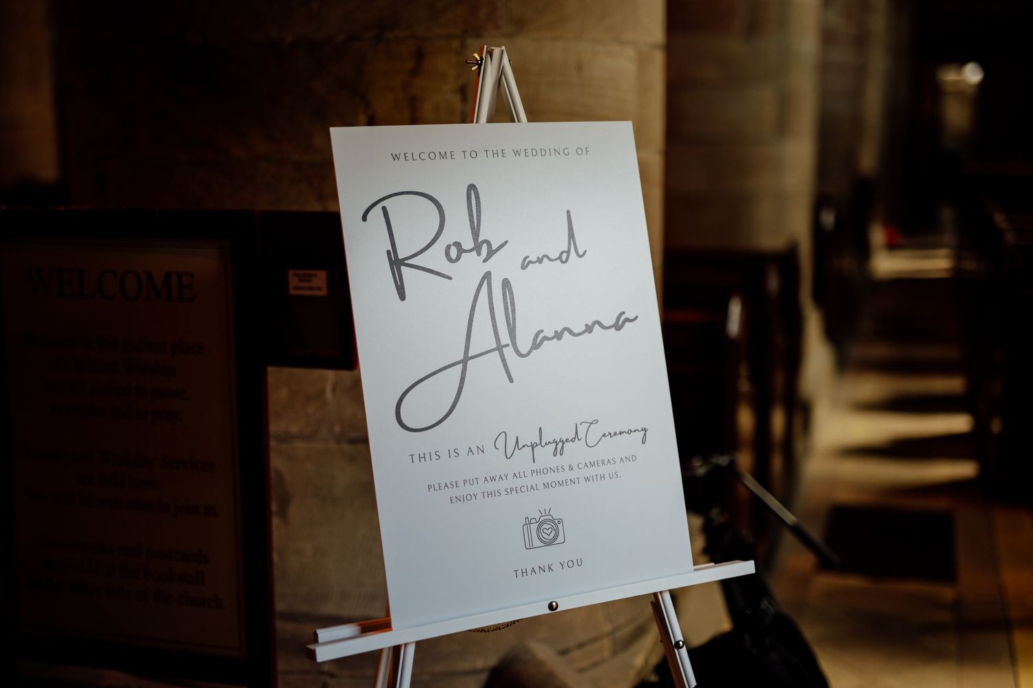 An elegant wedding welcome sign displayed on a wooden easel in rustic venue lighting.