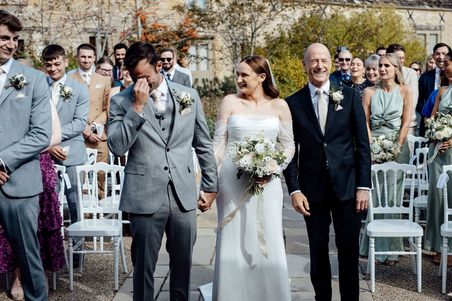 Wedding party and guests gather outdoors at a stone venue for a celebration ceremony.