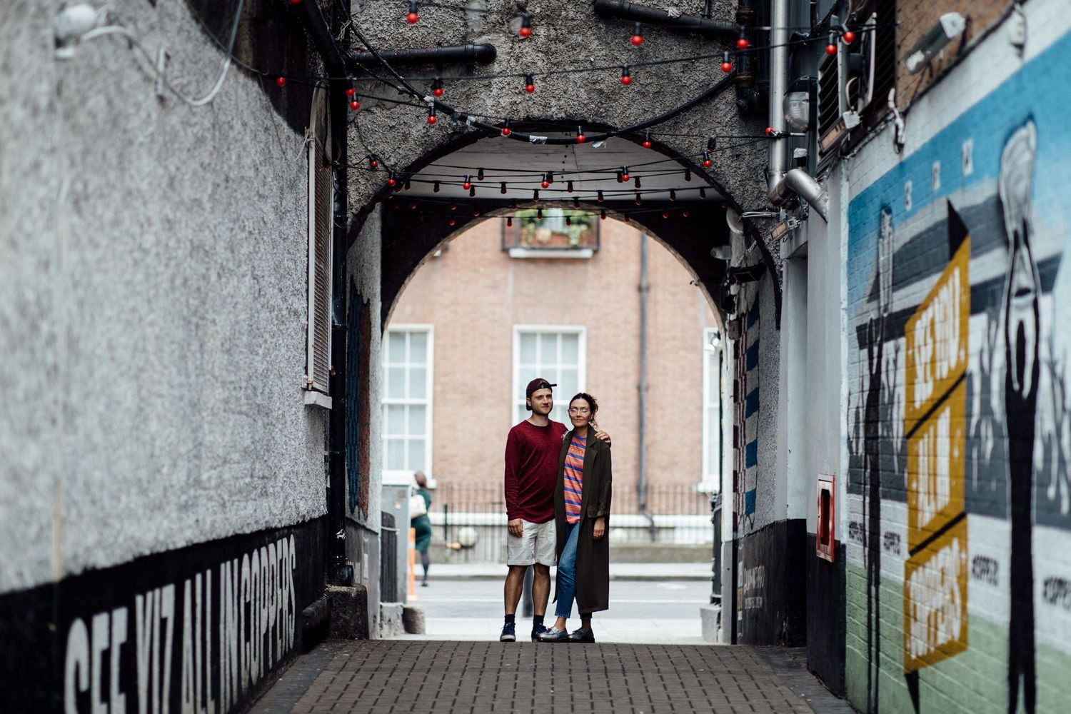 Urban alleyway with graffiti covered walls and distant figures walking.