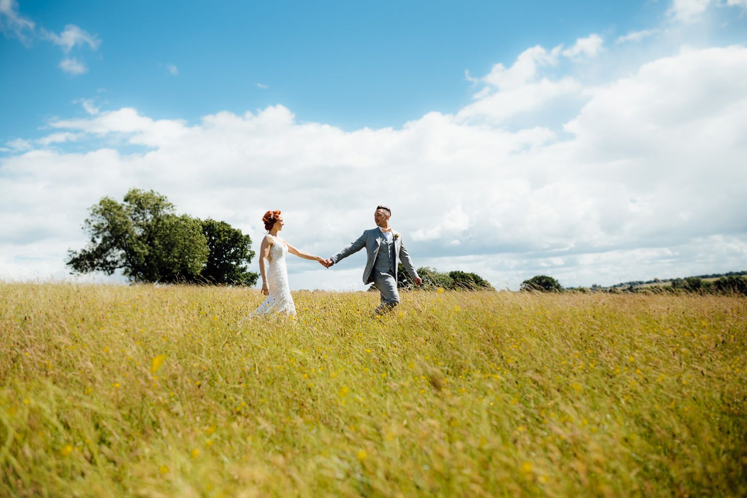 A couple runs joyfully through a golden wheat field under blue summer skies.