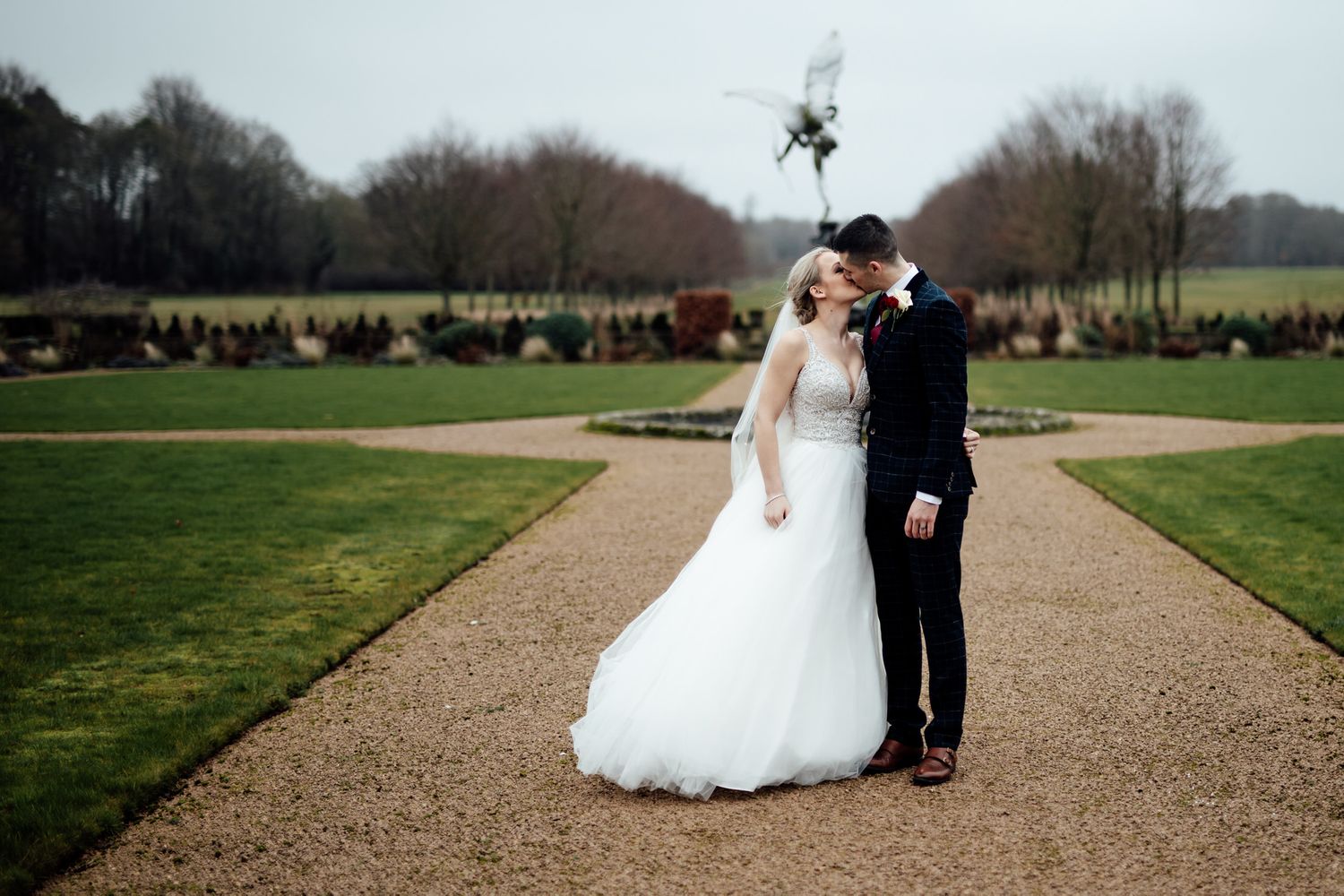 Wedding couple walking along a manicured gravel path surrounded by scenic grounds.