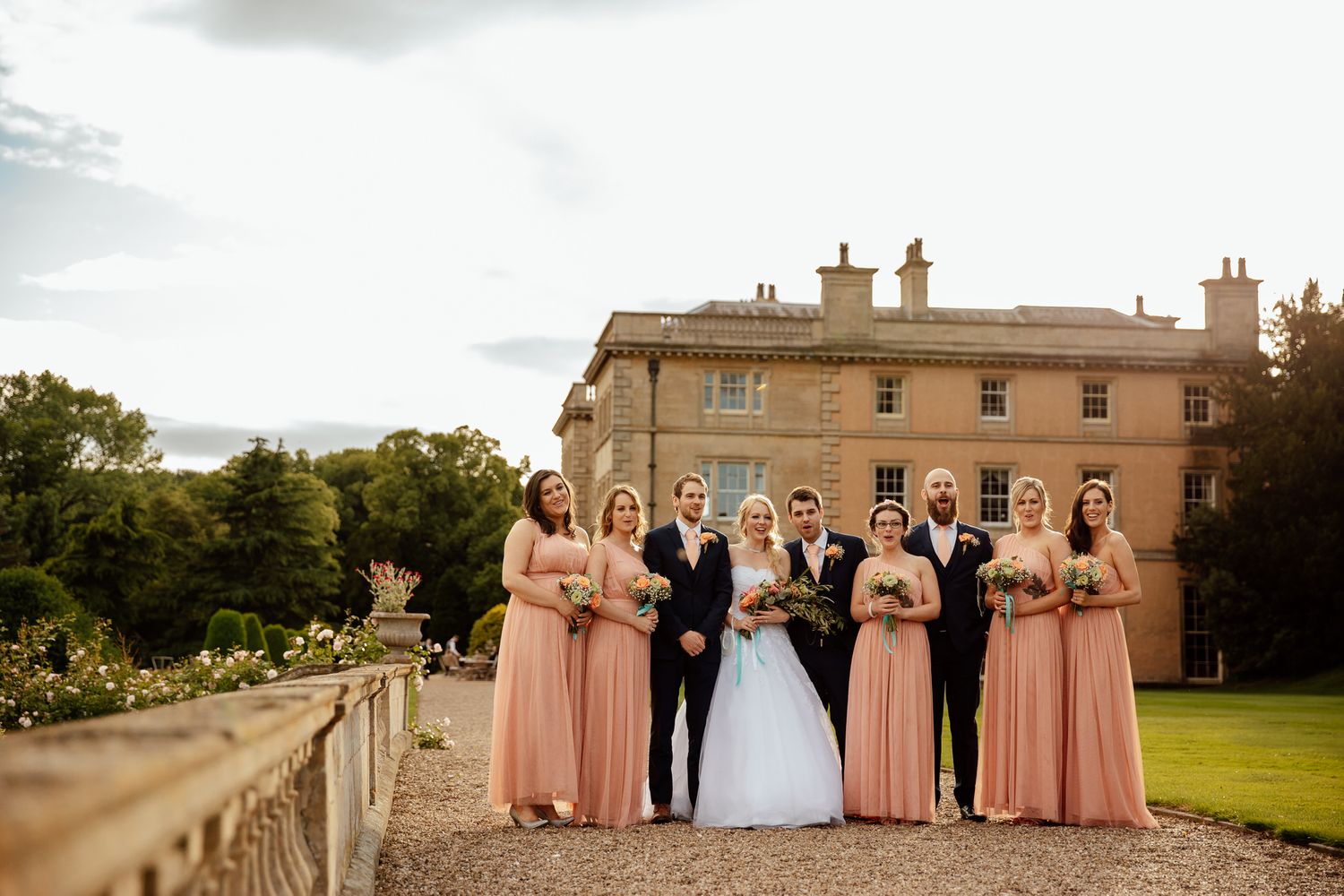 Grand stone mansion serves as backdrop for wedding party on sprawling lawn.