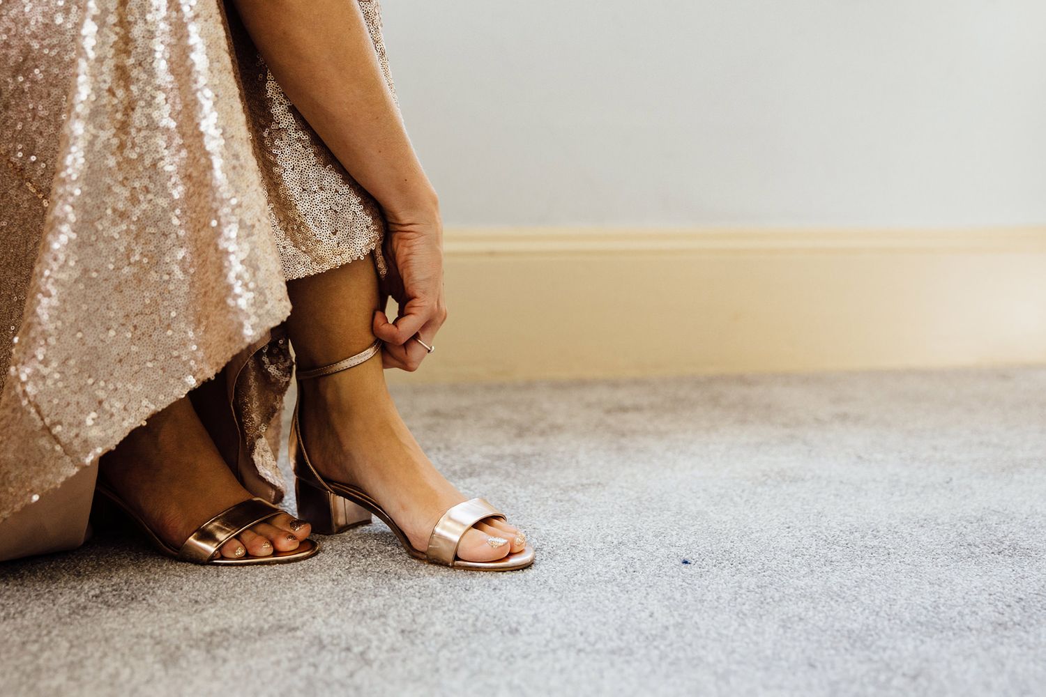 Close-up of sparkly gold sequin dress details and sandals on a light floor.