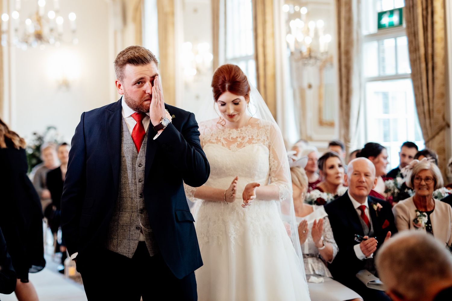 Elegant wedding reception in a bright ornate room with guests mingling and socializing.