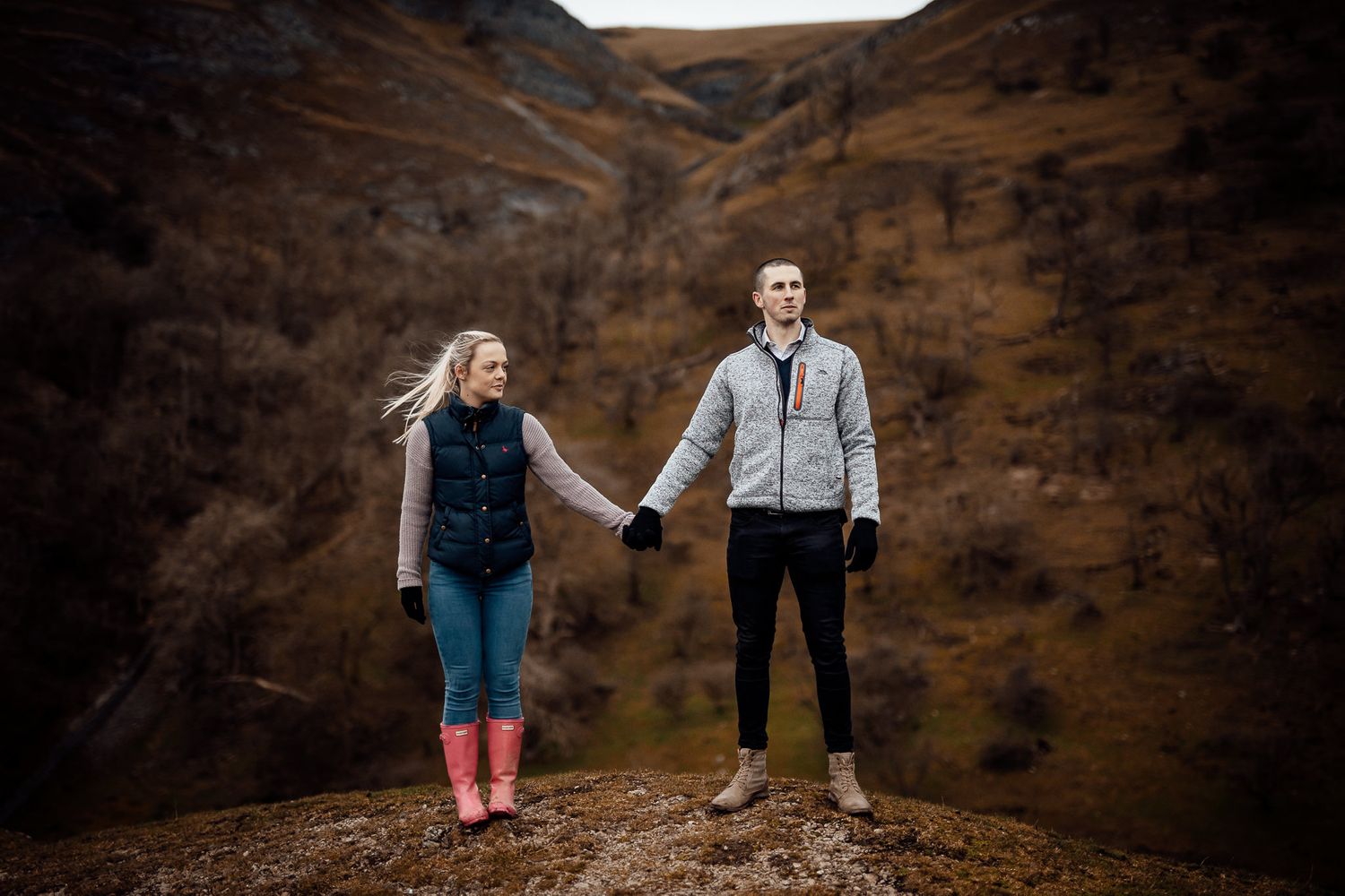 Two people embrace while standing on rugged mountain terrain at sunset.