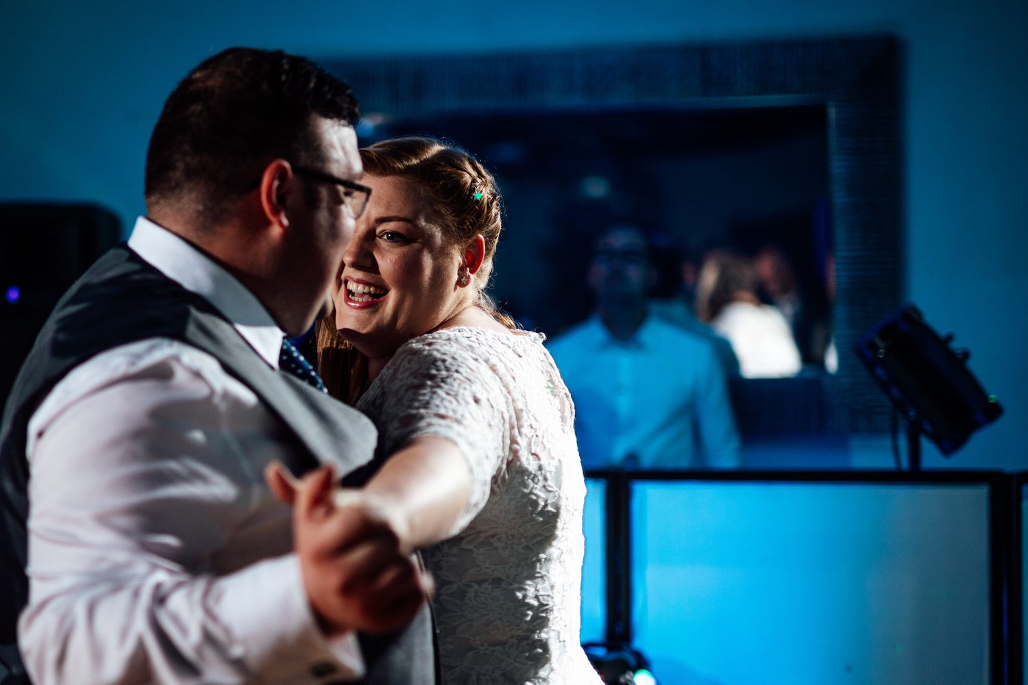 Couple dancing in spotlight with blue ambient lighting at wedding reception.
