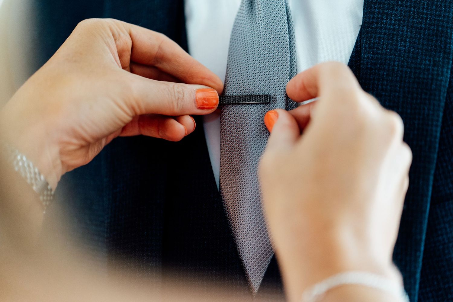 Hands adjusting gray tie during wedding preparations.