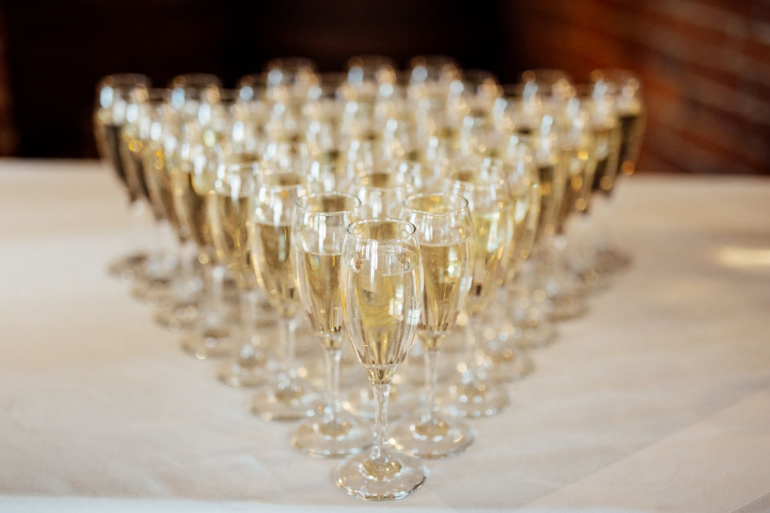 Rows of champagne flutes lined up on white tablecloth for wedding toast.