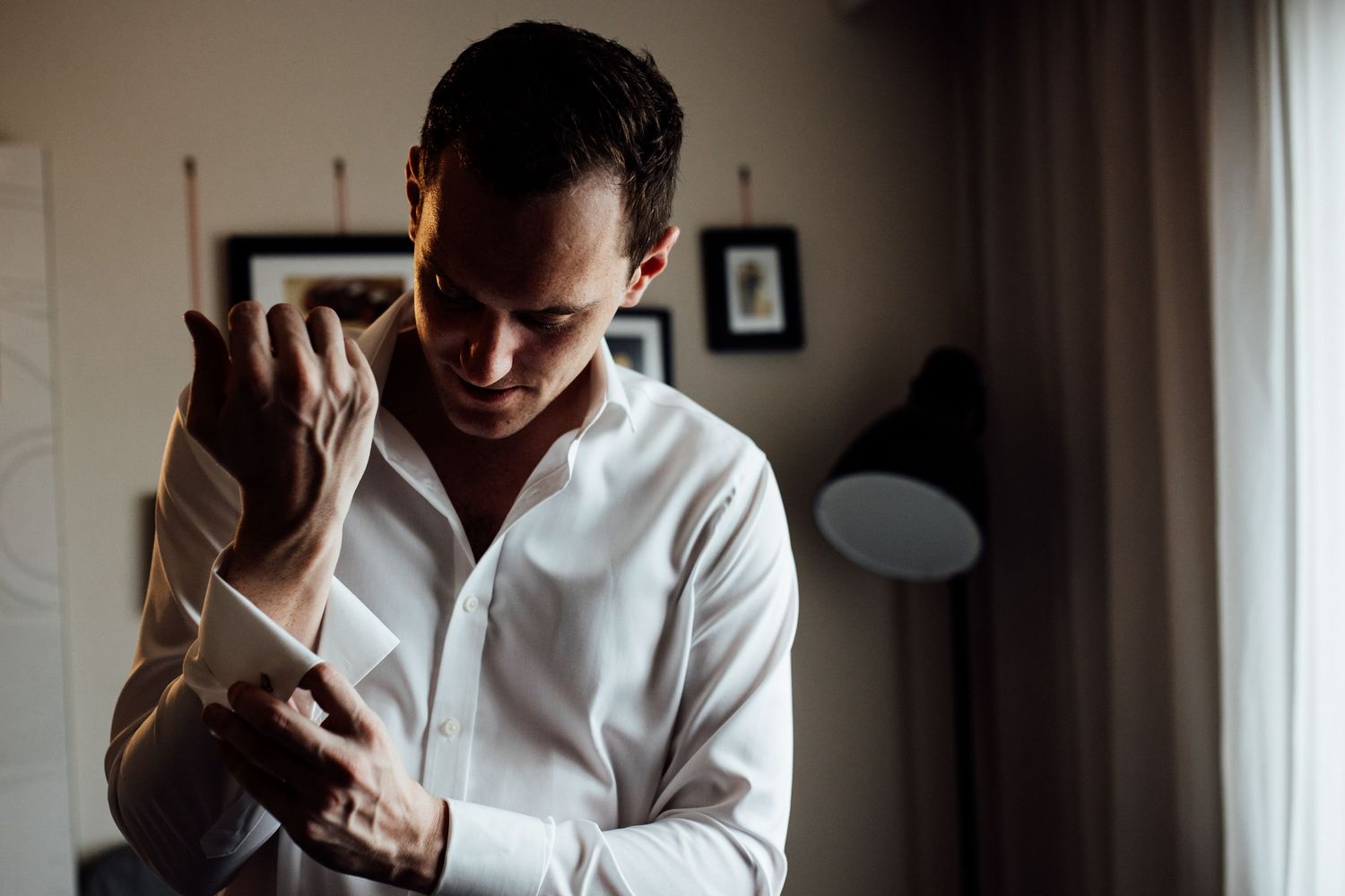 A person adjusting their cufflinks while getting ready in a dimly lit room.