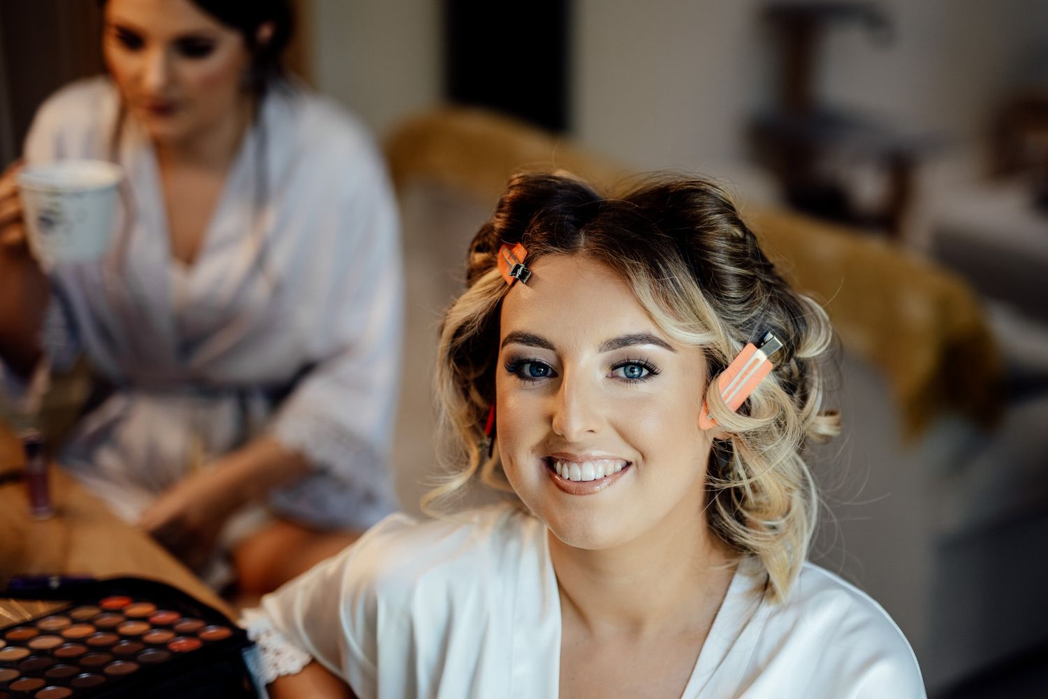 Bride getting ready with hair and makeup done in a white robe.