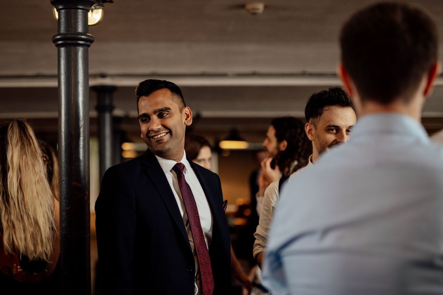 Wedding guests socializing during evening reception under indoor lighting.