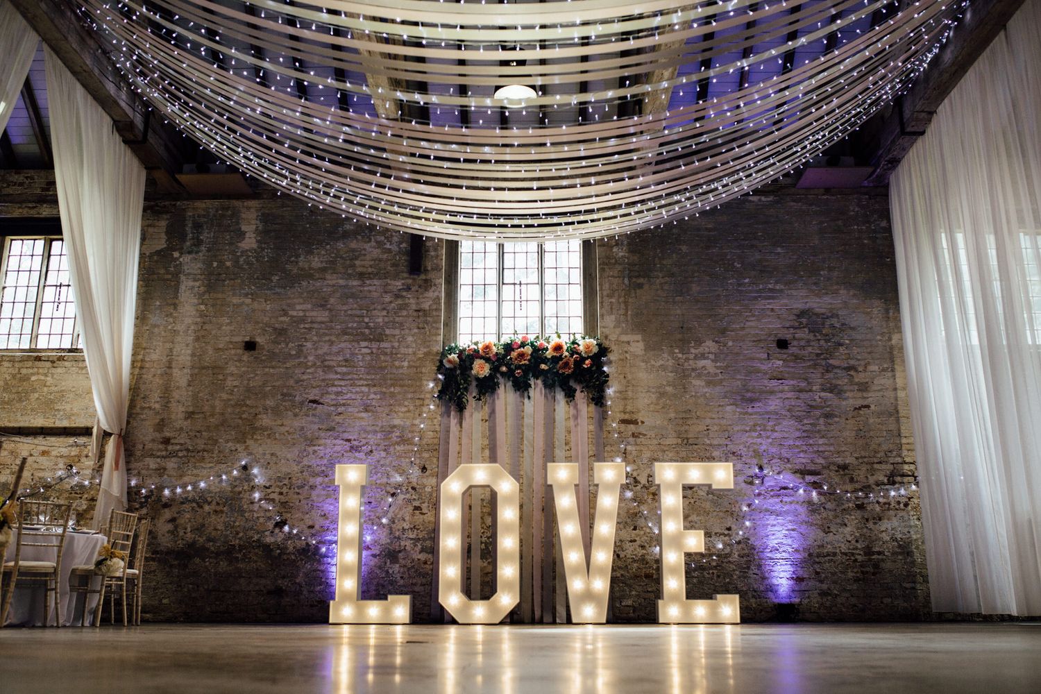Large illuminated LOVE letters and string lights decorate an industrial brick venue space.