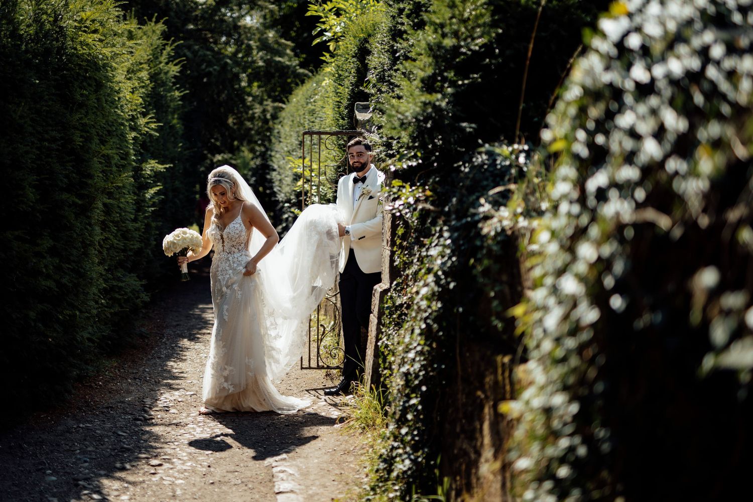 A wedding couple walking through a lush garden path with natural greenery.