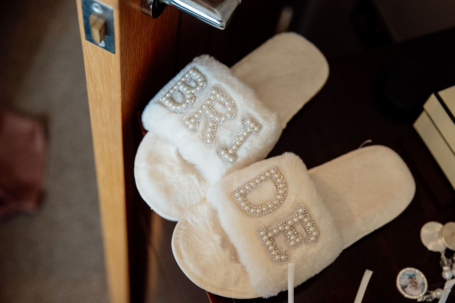 White bridal slippers with pearl embellishments displayed on a wooden surface.