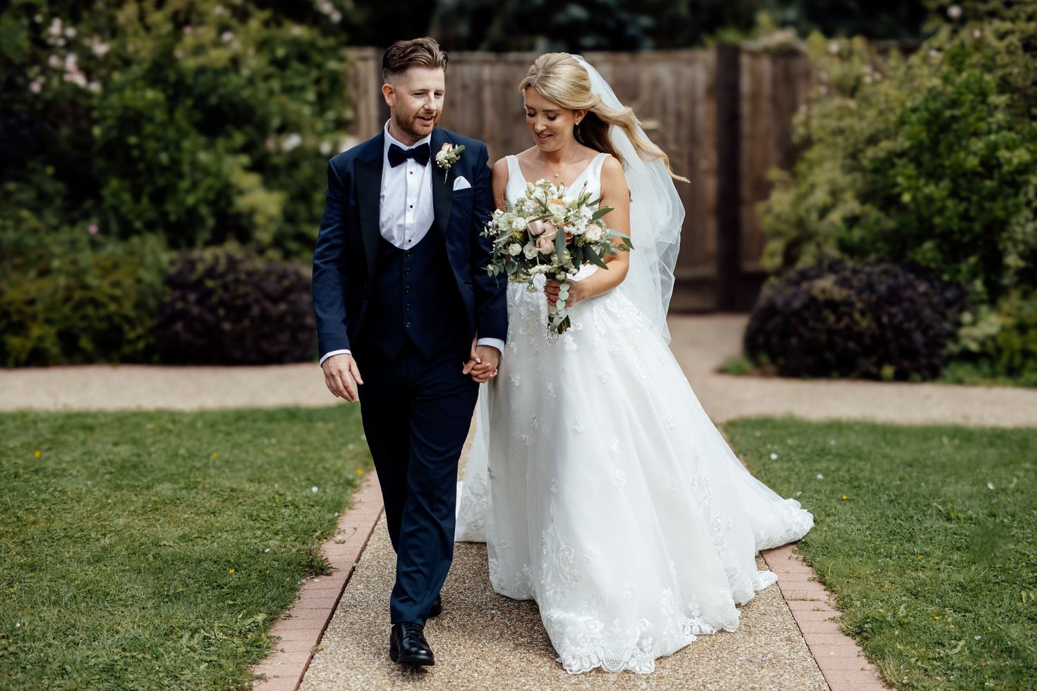 Couple walking together on garden path in formal wedding attire.
