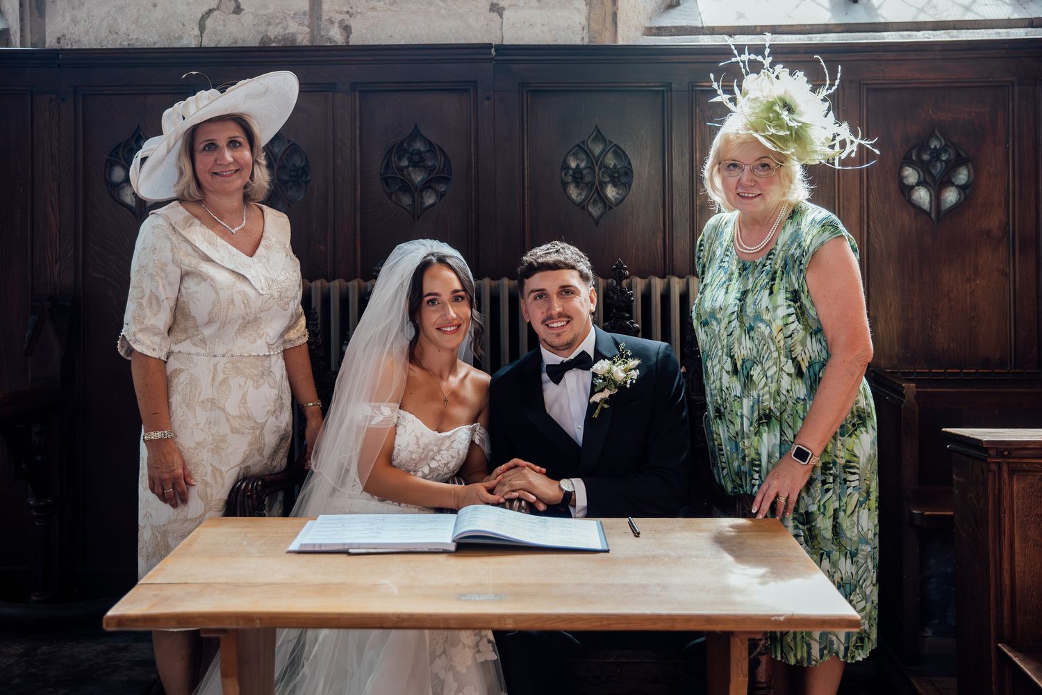 Wedding ceremony guests gather around table to sign marriage documents in traditional wood-paneled room.