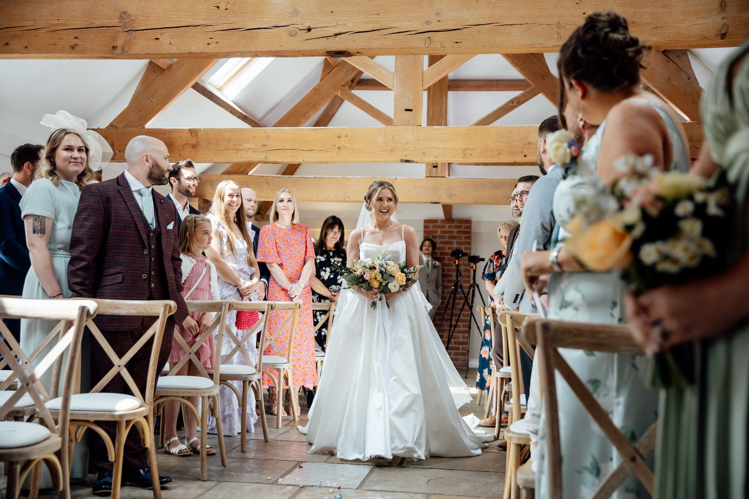Wedding reception setup in a rustic wooden barn with cross-back chairs and string lights.