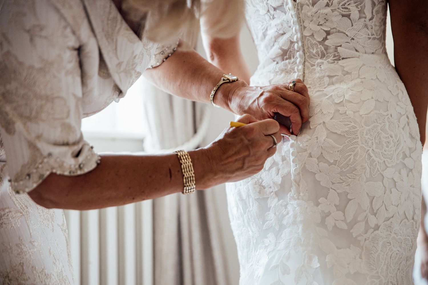 Close-up details of lace wedding dress and hands during ceremony.