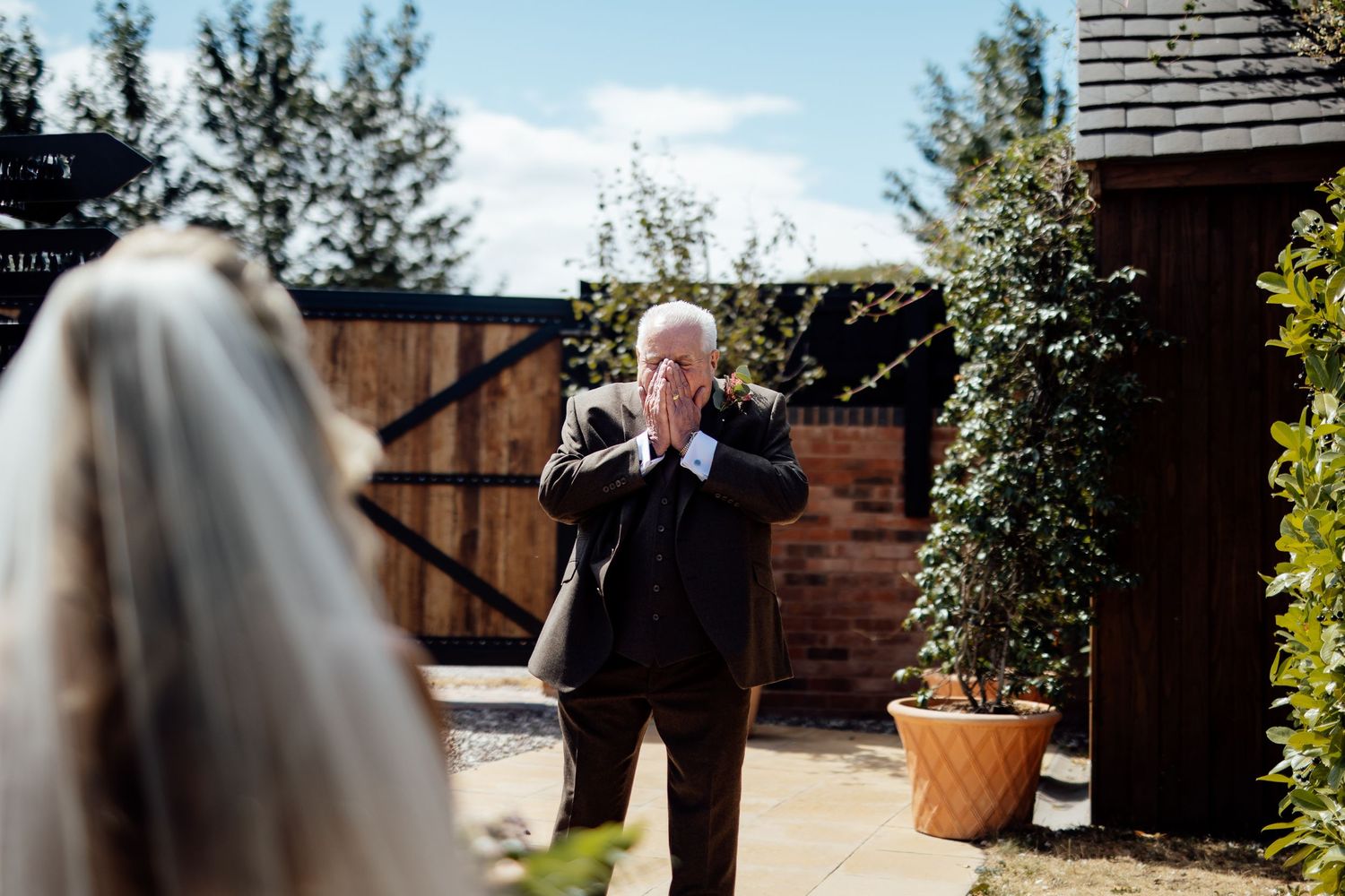 Emotional father clasps hands seeing bride in wedding veil for the first time at outdoor venue.