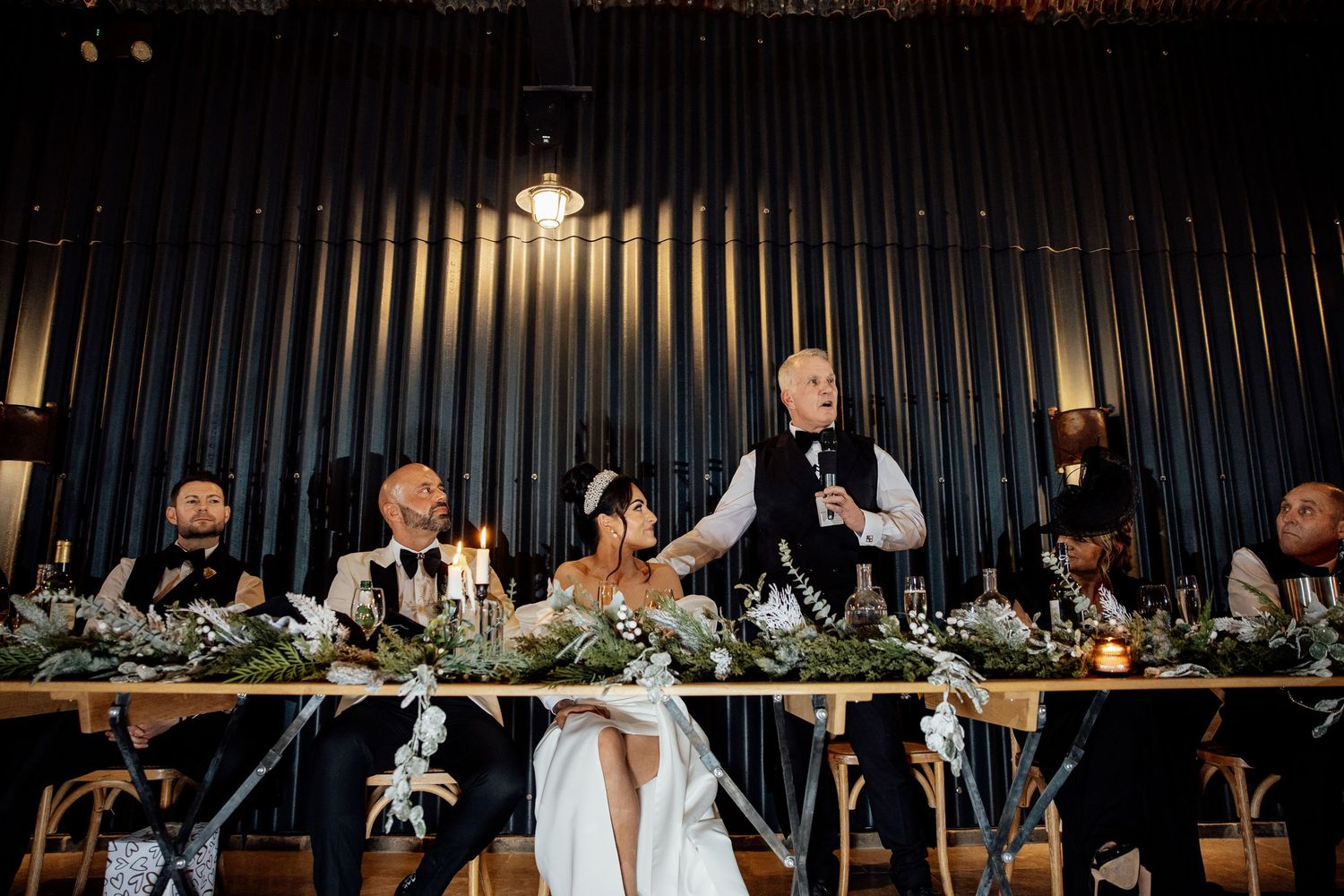 Wedding reception venue with dramatic black curtains and elegant table settings illuminated by warm lighting.
