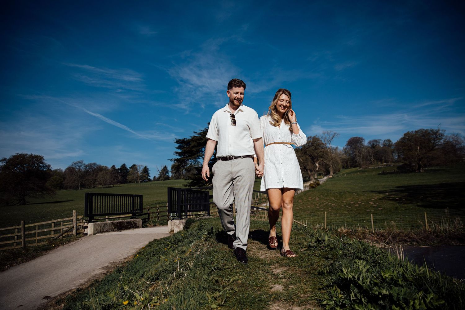 Two people in coordinating white outfits walking together on a countryside path.