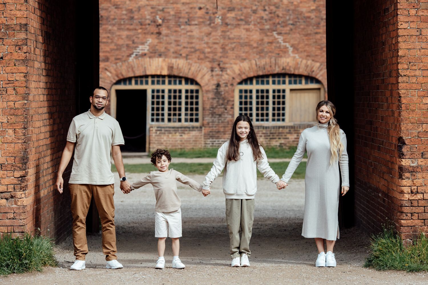 A family in coordinated white outfits poses together against a brick archway background.