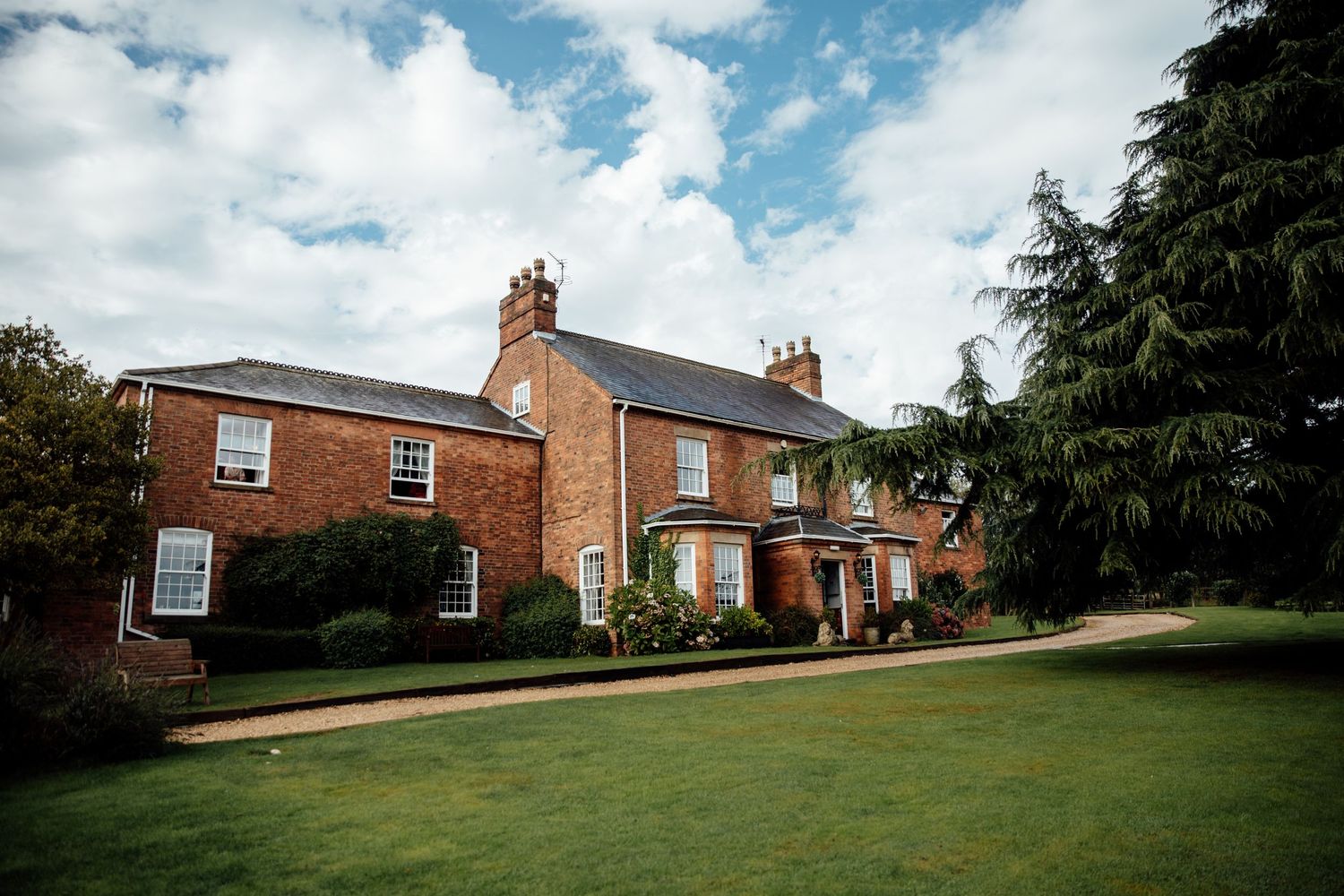 Exterior view of a traditional red brick building with landscaped grounds on a cloudy day.