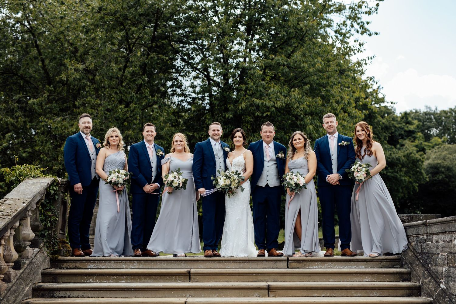 Wedding party in navy and grey attire posed on stone steps outdoors.