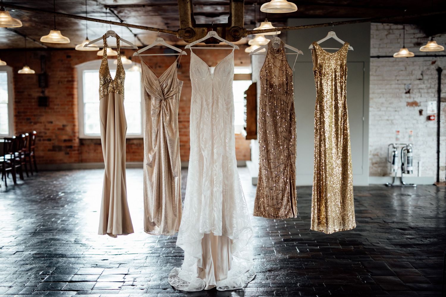 Wedding dresses hanging on display in an industrial-style room with exposed brick walls.