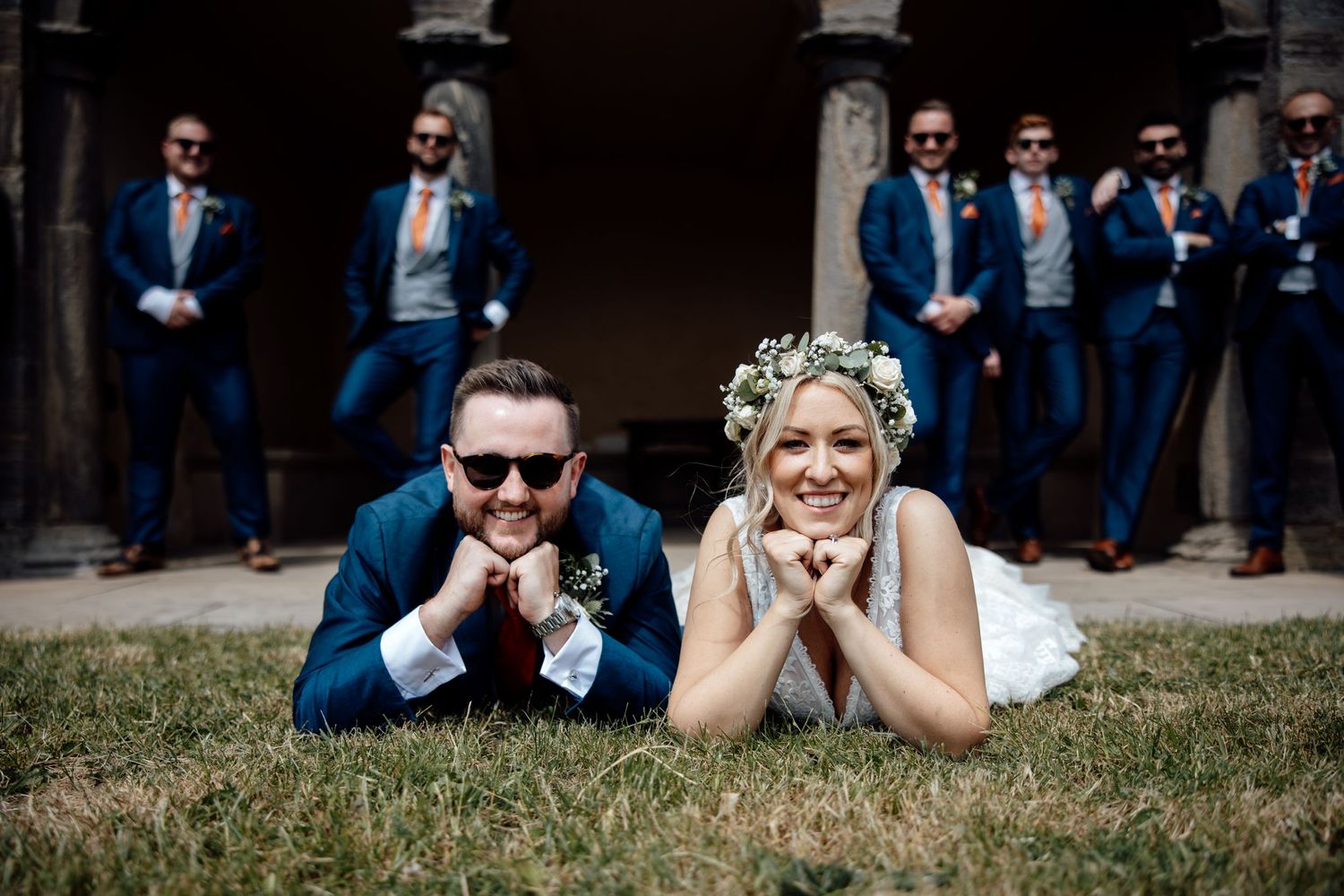 Wedding party poses playfully on grass outside historic building.