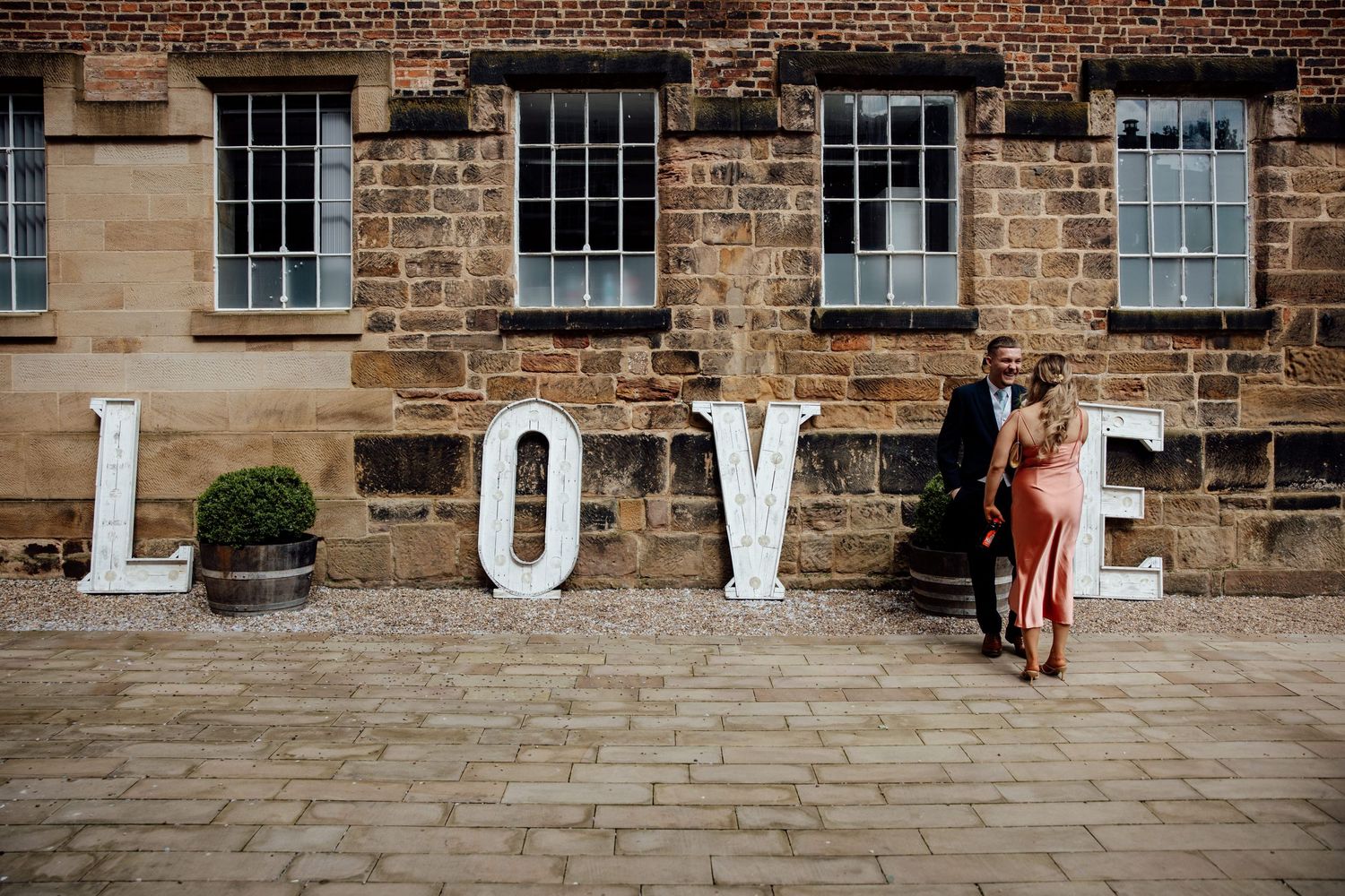 Couple posing against brick wall with large white LOVE letters.