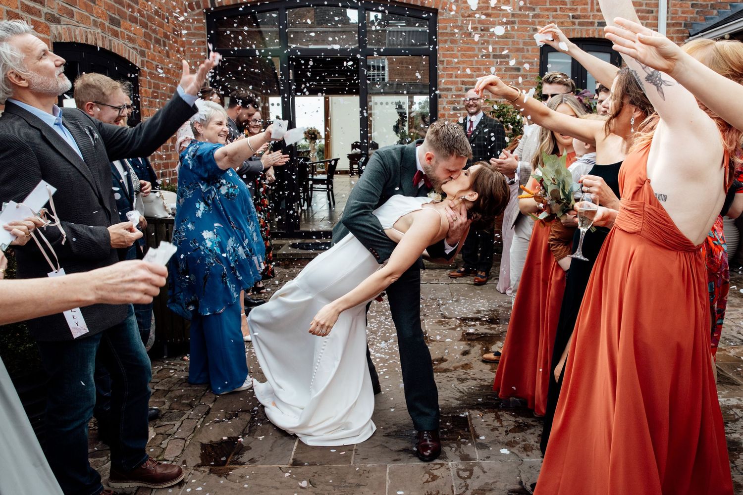 Wedding party celebrating outdoors near brick building with confetti.