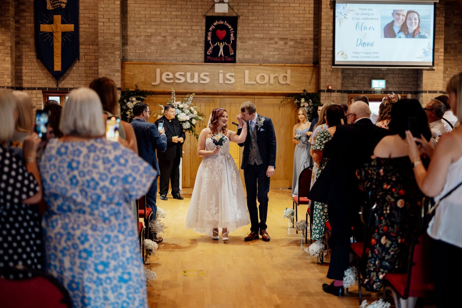 Wedding ceremony in progress inside a church with projected screens and gathered guests.