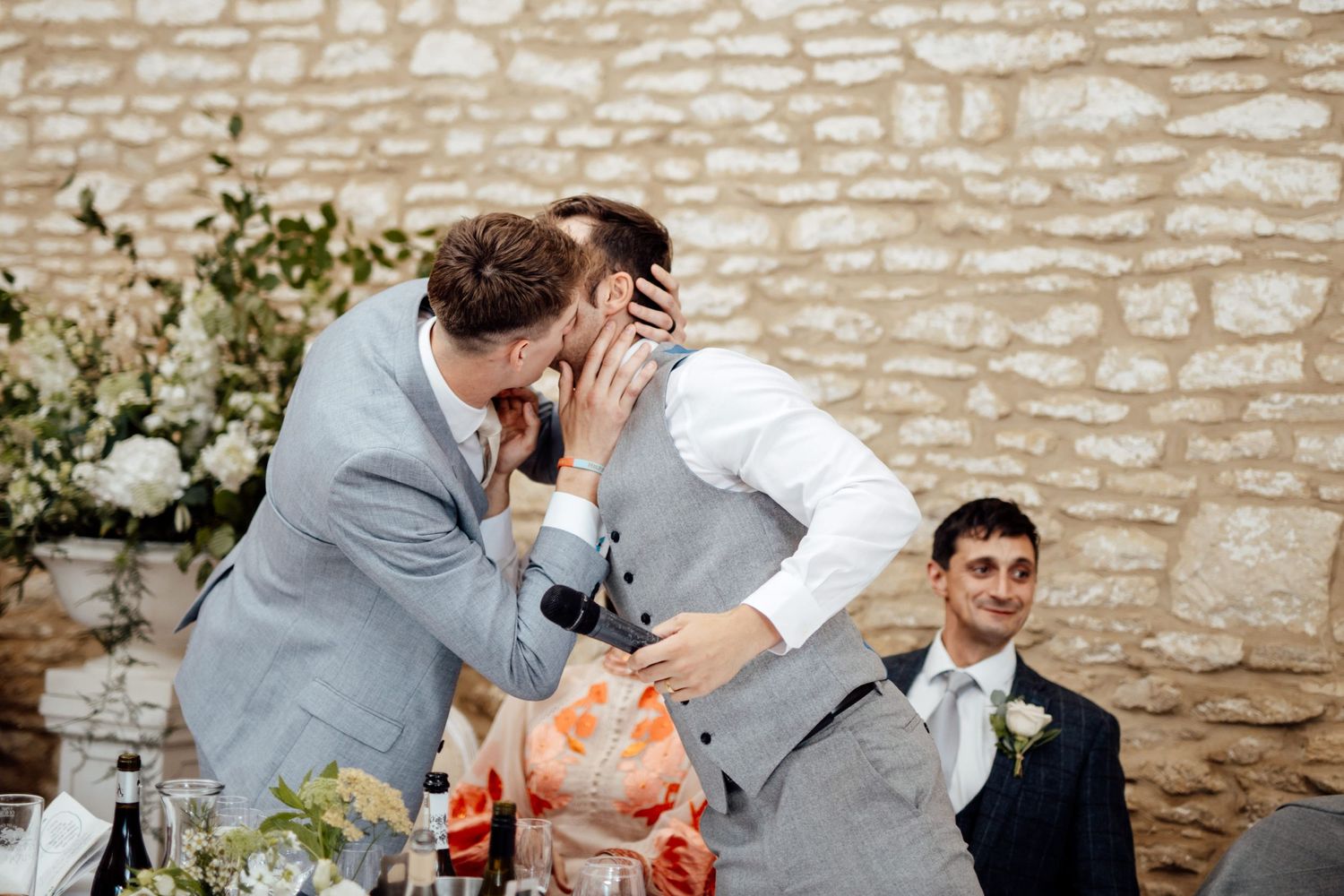 Emotional reactions during wedding speeches in rustic stone venue with floral decorations.