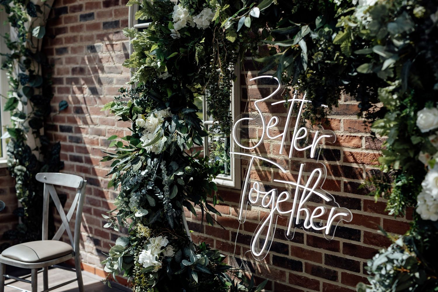 Rustic brick wall decorated with greenery and elegant handwritten signage.