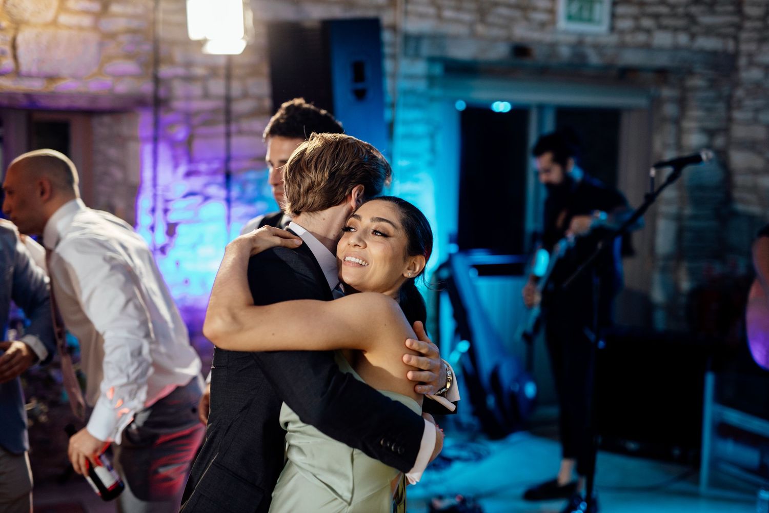 Couples dancing at a wedding reception with blue mood lighting in a rustic stone venue.