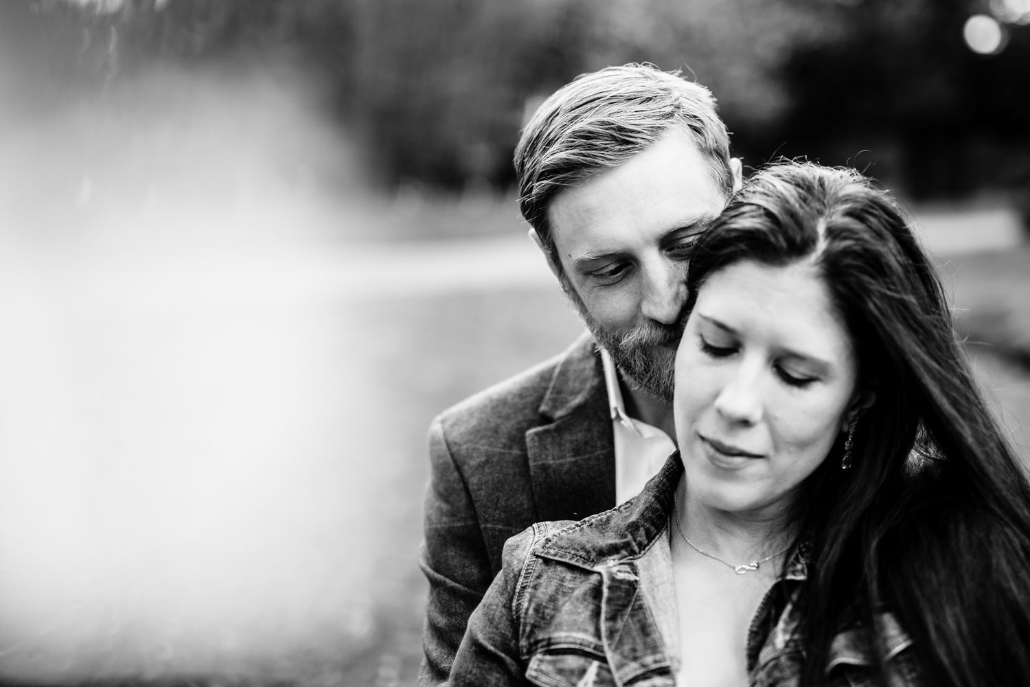 Black and white intimate portrait of a couple sharing a tender moment outdoors.