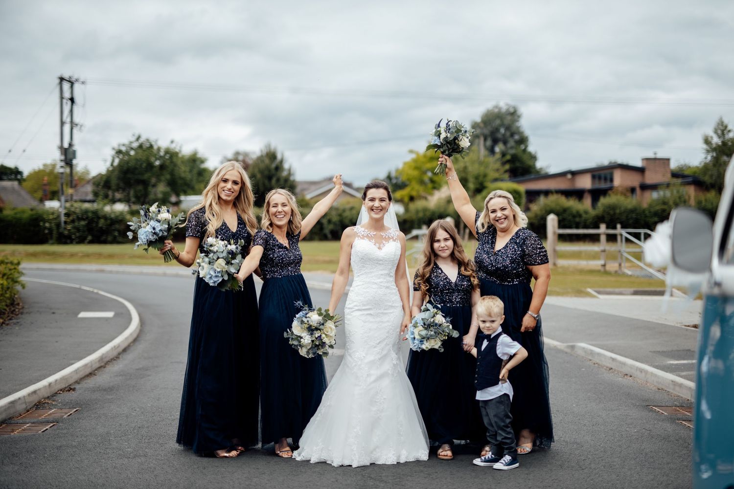 Wedding party gathers for a fun group photo on a suburban street.