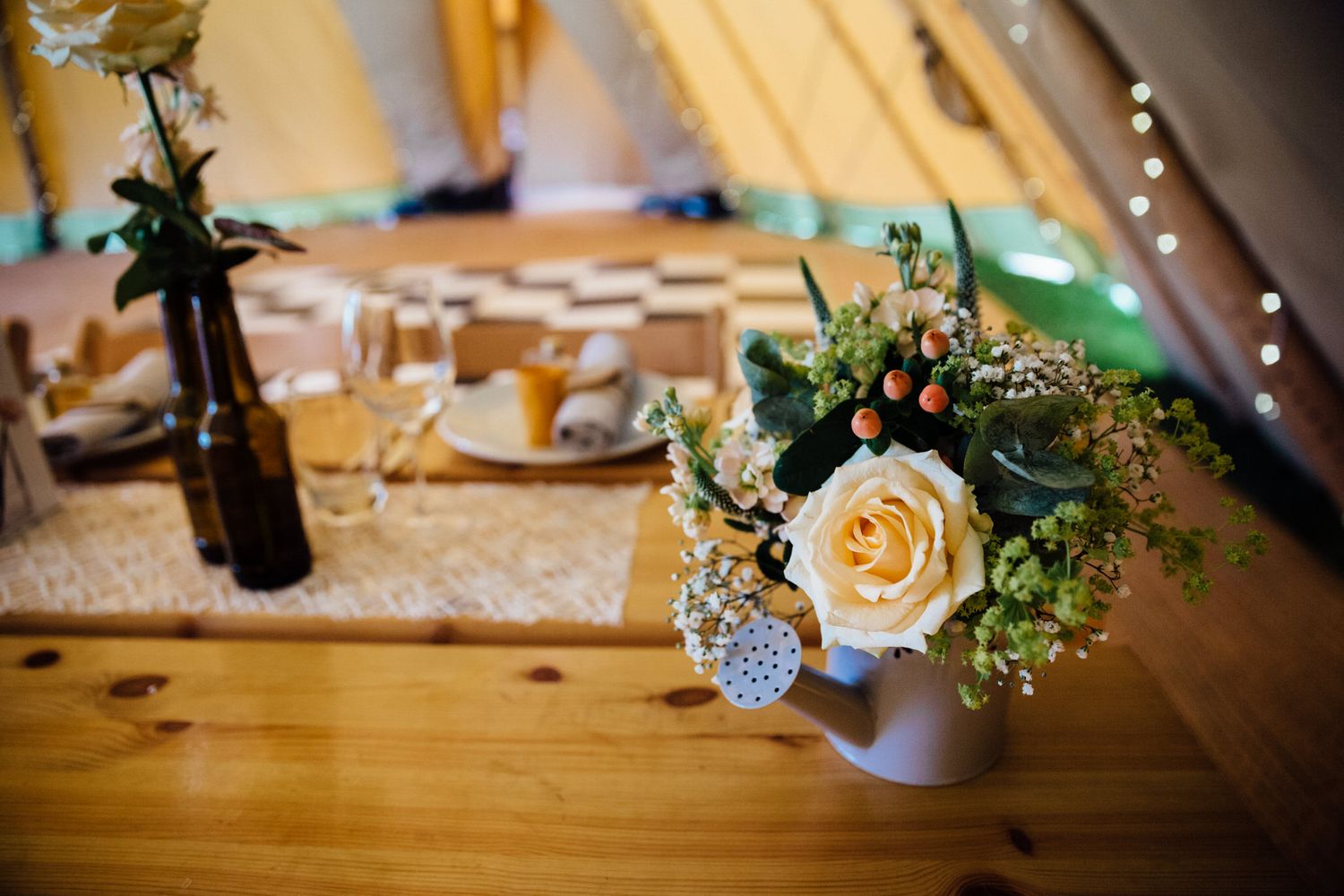 Delicate yellow roses and floral arrangements decorate wooden tables at a wedding reception.